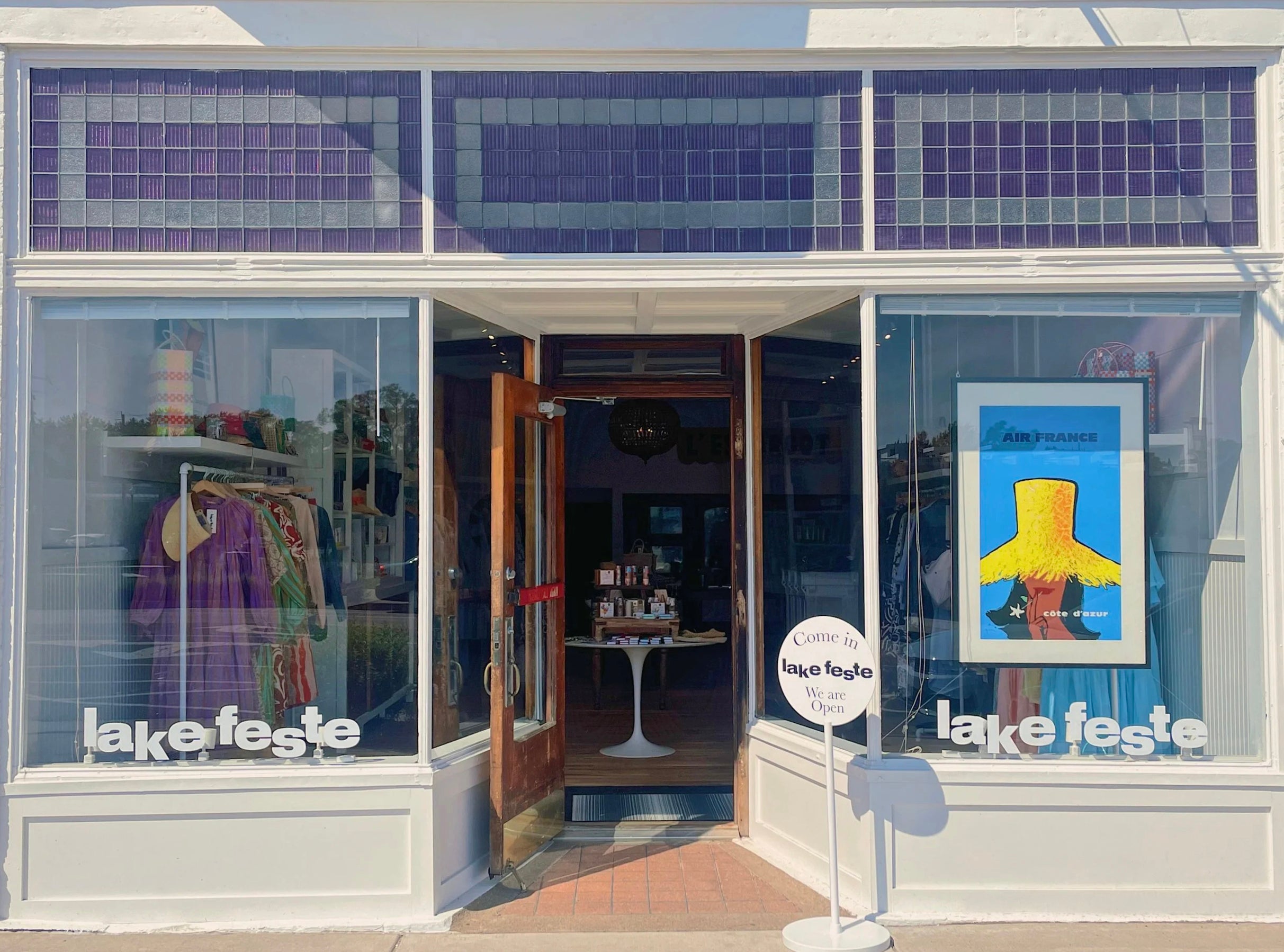 Storefront with 'lake feste' branding, clothing displayed, and a poster on the window.