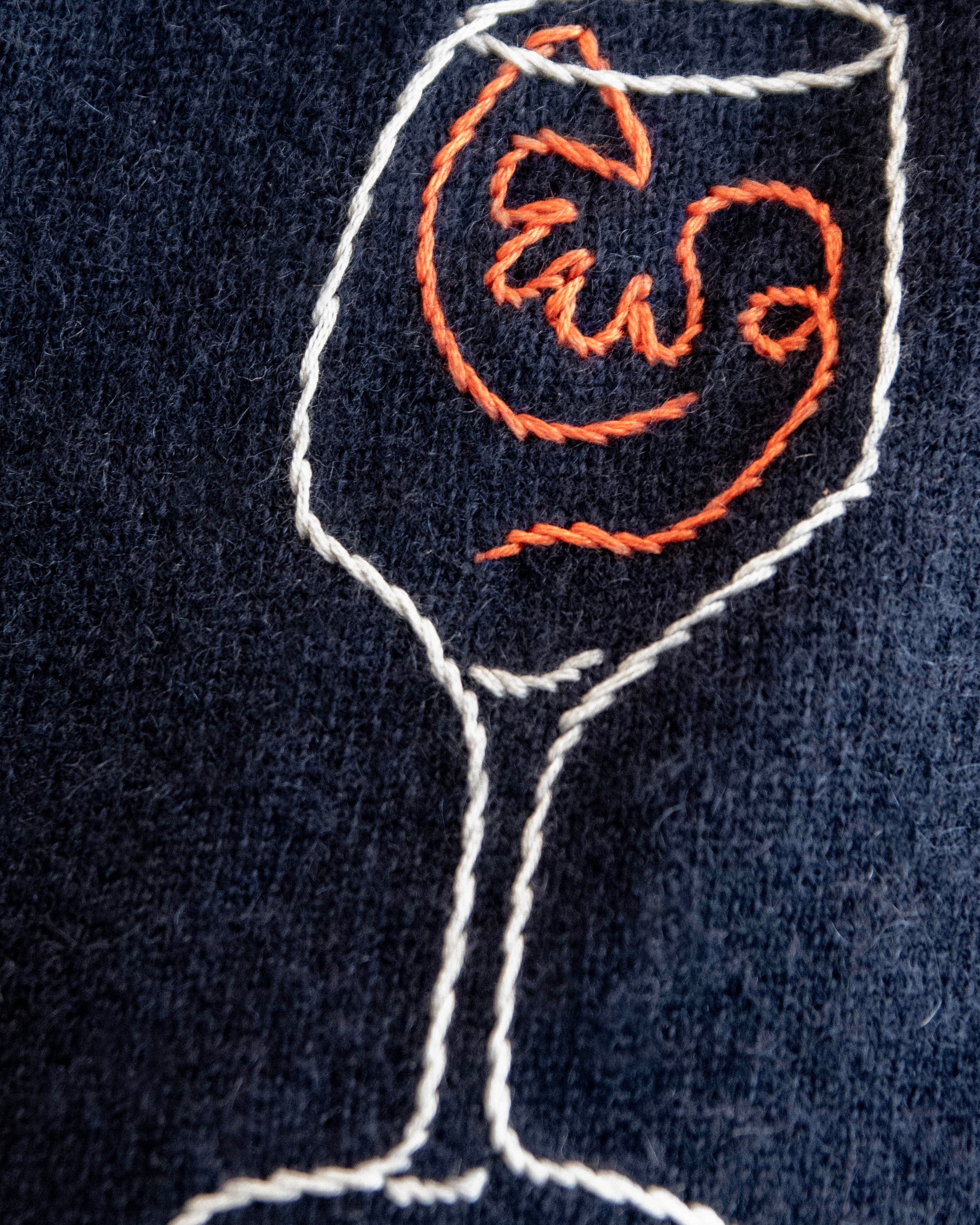 Embroidered design of a cocktail glass with a shrimp on a dark fabric background