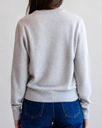 Person wearing a light gray sweater and blue jeans against a plain background